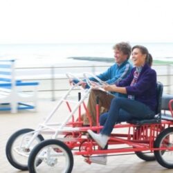 Twee vakantiegangers lachend en duidelijk genietend van hun tochtje op de zeedijk met de go-cart