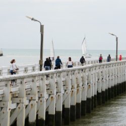 Uitvarende zeilboten en wandelaars die een eindje de zee ingaan op de staketsels van Nieuwpoort