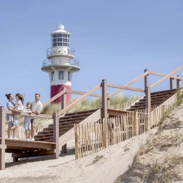 Vakantiegangers op de houten trap over de duinenrij bij de vuurtoren genietend van het uitzicht op het nieuwe strandreservaat